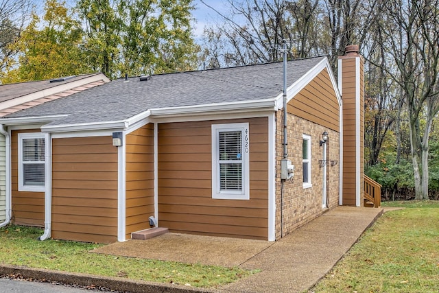 view of side of home with roof with shingles, brick siding, a chimney, and a lawn