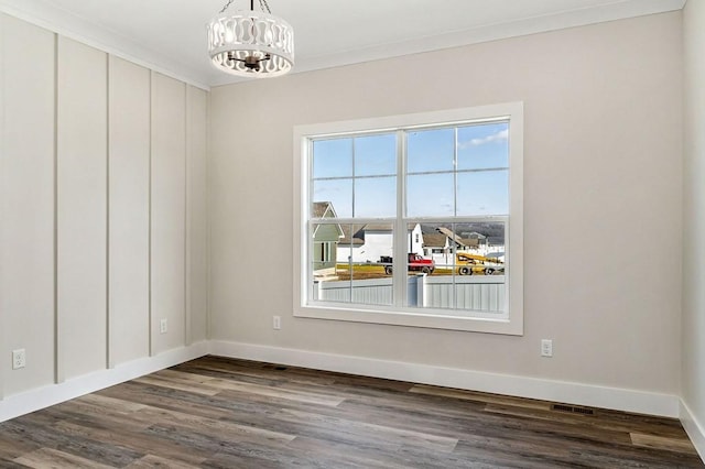 spare room featuring dark wood-type flooring, ornamental molding, and a chandelier