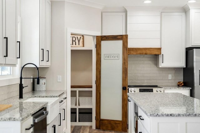 kitchen featuring white cabinetry, stainless steel appliances, light stone countertops, and backsplash