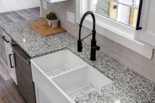 room details featuring dishwasher, sink, white cabinets, light stone countertops, and dark wood-type flooring