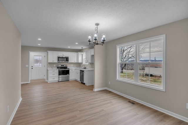 kitchen with stainless steel appliances, white cabinetry, light hardwood / wood-style floors, and decorative light fixtures