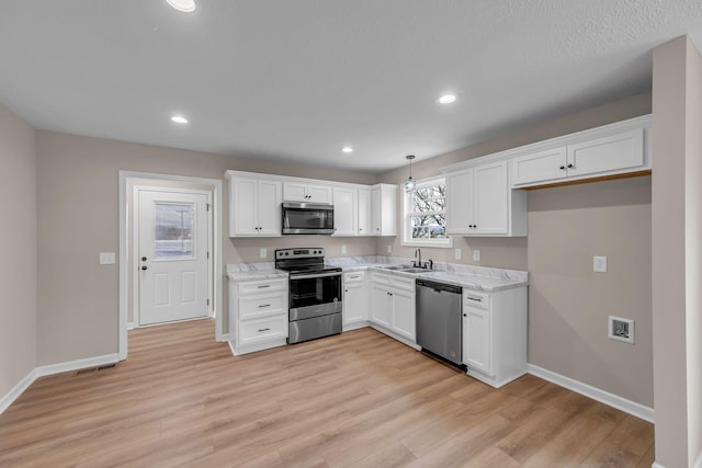 kitchen with white cabinetry, appliances with stainless steel finishes, pendant lighting, and light hardwood / wood-style flooring