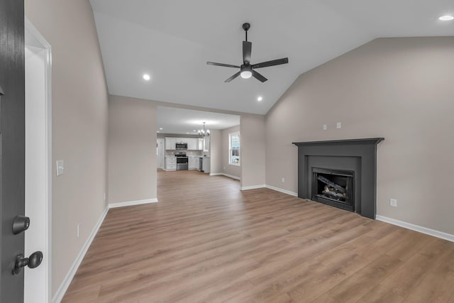 unfurnished living room featuring ceiling fan with notable chandelier, vaulted ceiling, and light wood-type flooring