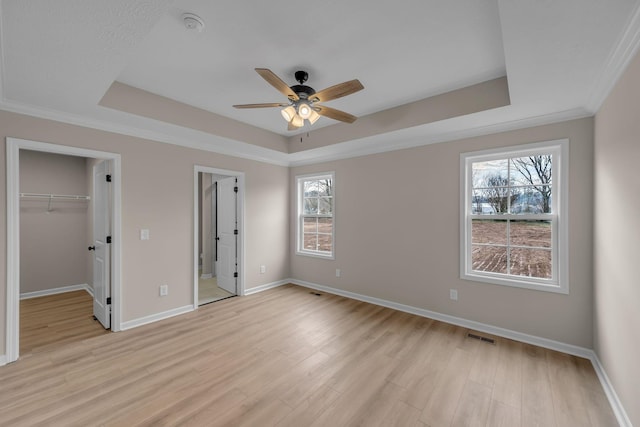 unfurnished bedroom with ensuite bath, light hardwood / wood-style flooring, a tray ceiling, ornamental molding, and a spacious closet