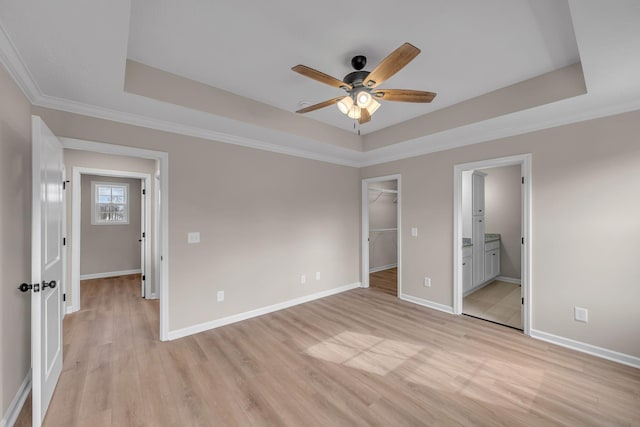 unfurnished bedroom with a walk in closet, ornamental molding, a raised ceiling, and light wood-type flooring