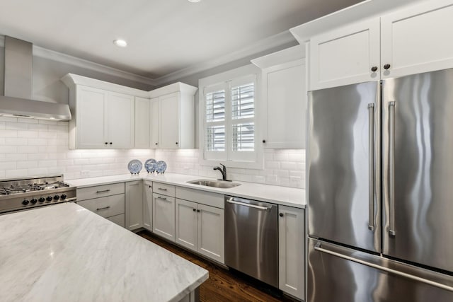 kitchen with appliances with stainless steel finishes, tasteful backsplash, white cabinetry, sink, and wall chimney exhaust hood