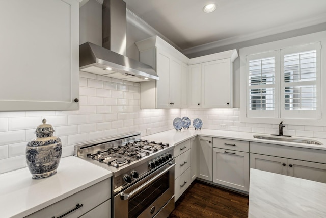 kitchen with wall chimney range hood, sink, backsplash, stainless steel range, and white cabinets