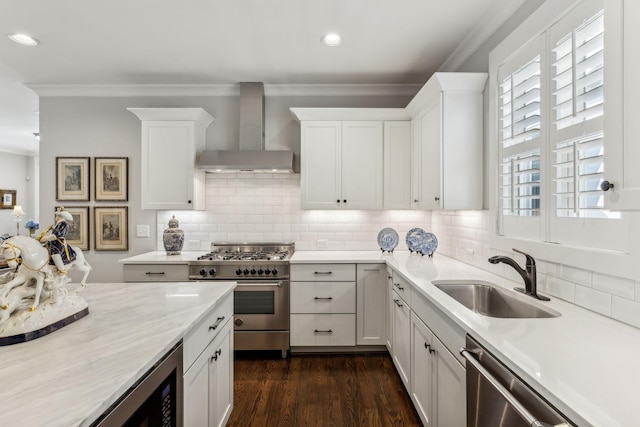 kitchen featuring appliances with stainless steel finishes, sink, white cabinets, ornamental molding, and wall chimney range hood