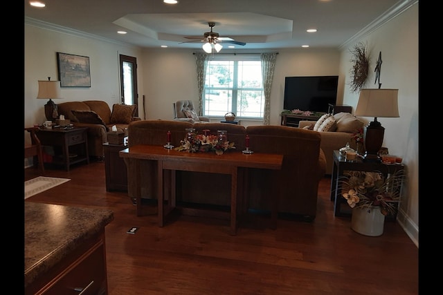 living room with ornamental molding, dark wood-type flooring, ceiling fan, and a tray ceiling