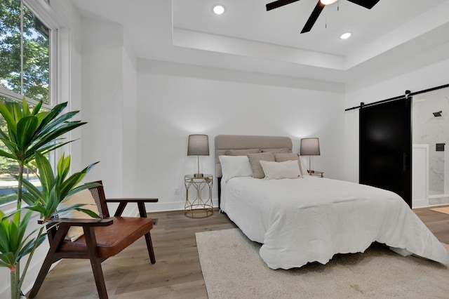 bedroom featuring ceiling fan, wood-type flooring, a barn door, and a raised ceiling