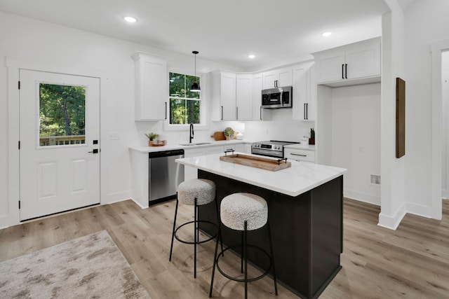 kitchen featuring sink, appliances with stainless steel finishes, hanging light fixtures, a center island, and white cabinets