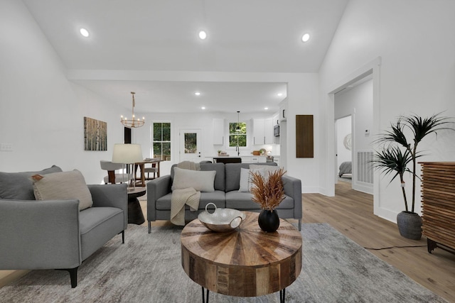 living room with an inviting chandelier, lofted ceiling, and light wood-type flooring