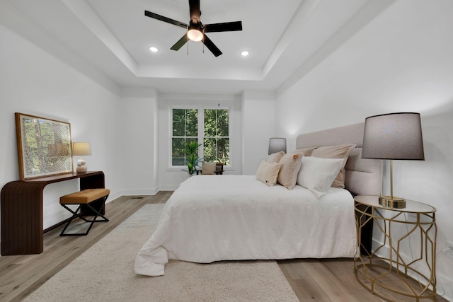 bedroom with a raised ceiling, ceiling fan, and light wood-type flooring