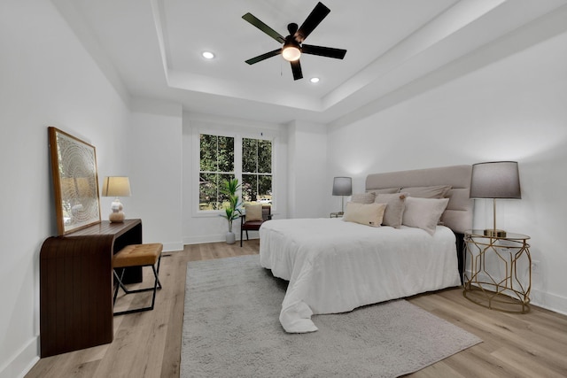 bedroom with ceiling fan, a tray ceiling, and light hardwood / wood-style floors