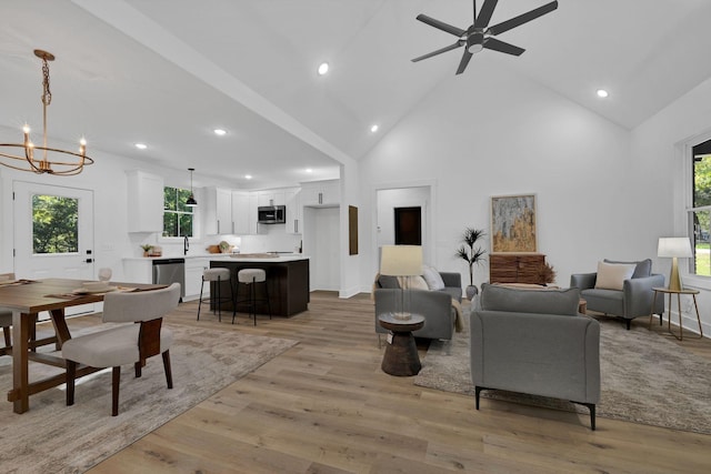 living room featuring sink, ceiling fan with notable chandelier, high vaulted ceiling, and light hardwood / wood-style flooring