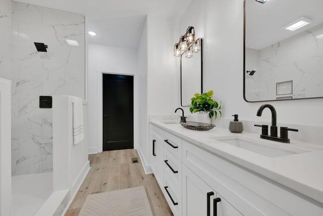 bathroom featuring wood-type flooring, tiled shower, and vanity