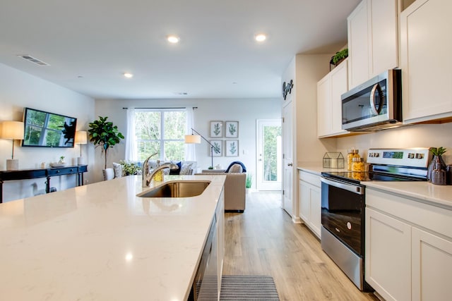 kitchen with sink, white cabinetry, light wood-type flooring, appliances with stainless steel finishes, and light stone countertops