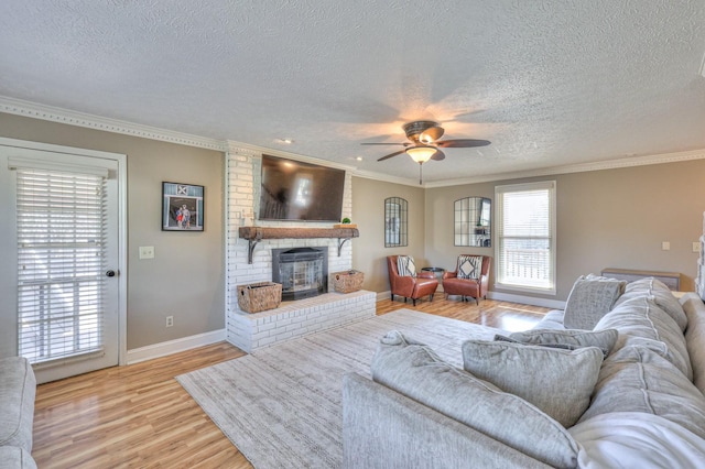 living room with a fireplace, light wood-type flooring, ornamental molding, ceiling fan, and a textured ceiling