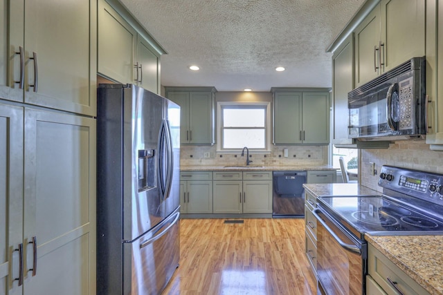 kitchen featuring sink, backsplash, light hardwood / wood-style floors, black appliances, and light stone countertops