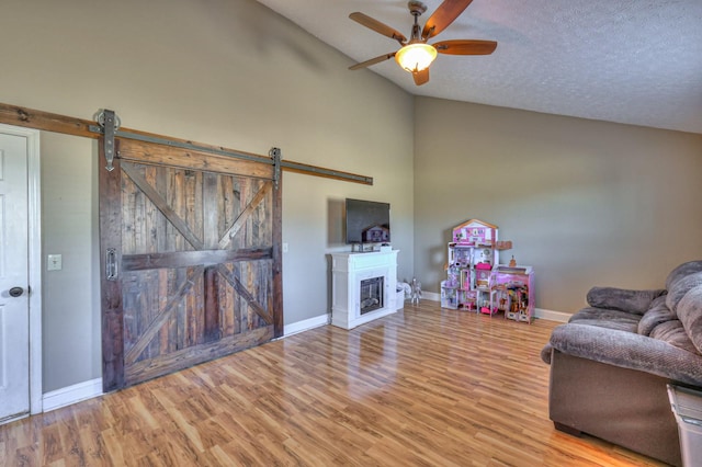 unfurnished living room with ceiling fan, a barn door, a textured ceiling, and light wood-type flooring