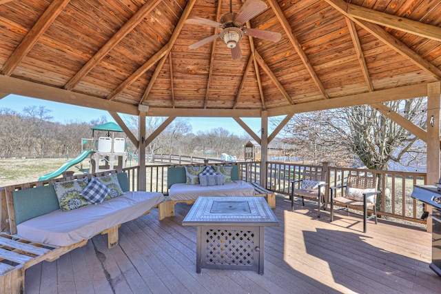 wooden terrace with a playground, a gazebo, an outdoor living space with a fire pit, and ceiling fan