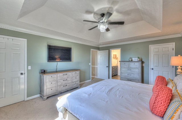 bedroom with crown molding, connected bathroom, light colored carpet, and a tray ceiling