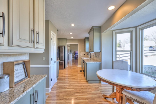 kitchen with stainless steel refrigerator, sink, gray cabinetry, light stone counters, and light hardwood / wood-style floors