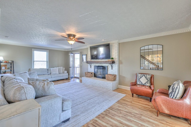 living room featuring ceiling fan, light hardwood / wood-style floors, crown molding, a brick fireplace, and a textured ceiling