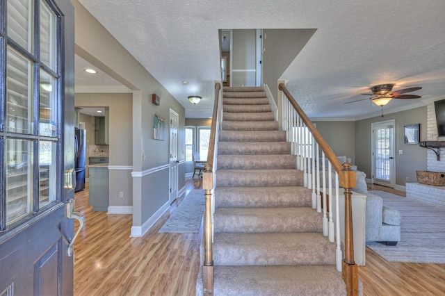 stairway with ornamental molding, wood-type flooring, and a textured ceiling