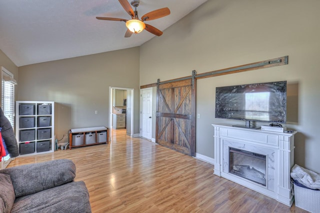 living room featuring light hardwood / wood-style flooring, high vaulted ceiling, a barn door, and ceiling fan