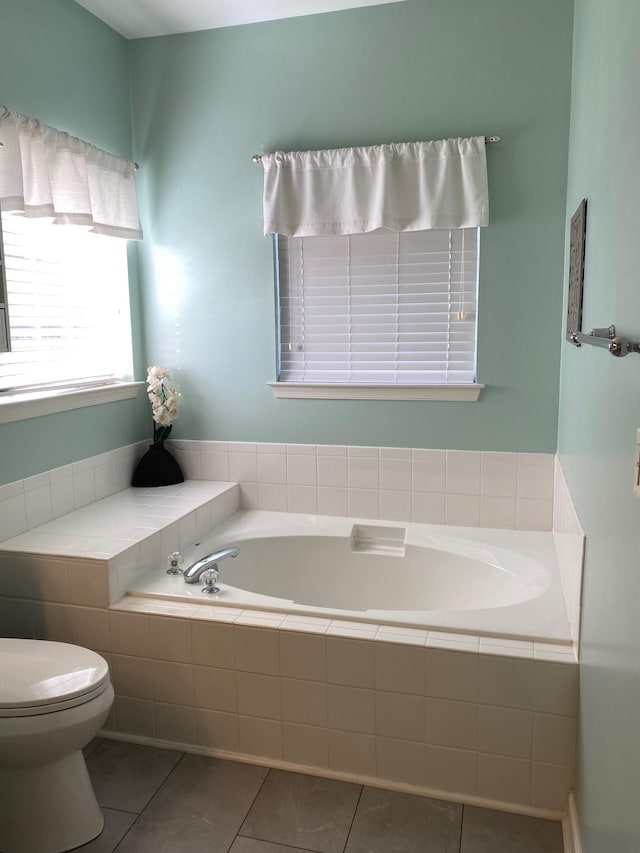 bathroom with tile patterned flooring, tiled tub, and toilet