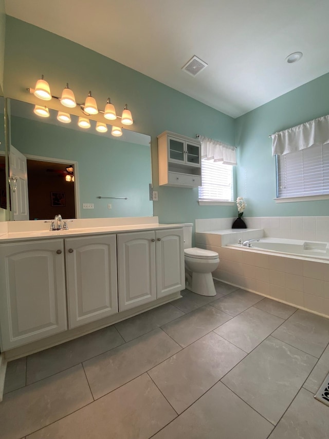 bathroom with vanity, a relaxing tiled tub, tile patterned floors, and toilet