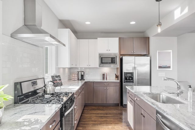 kitchen featuring pendant lighting, sink, appliances with stainless steel finishes, white cabinets, and wall chimney exhaust hood