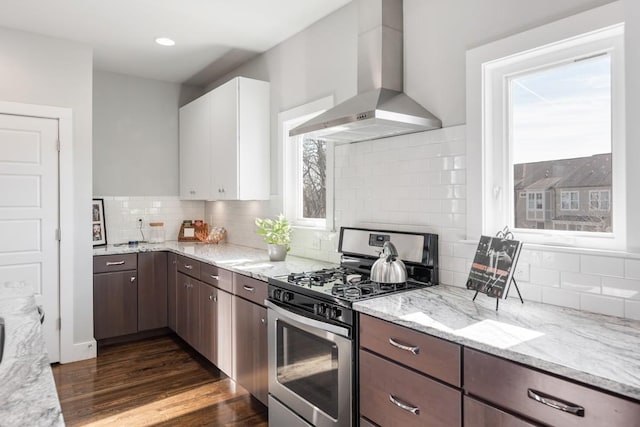 kitchen featuring wall chimney range hood, white cabinetry, stainless steel range with gas stovetop, light stone counters, and dark brown cabinetry