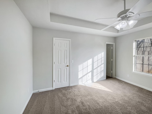 empty room with a tray ceiling, ceiling fan, and carpet flooring