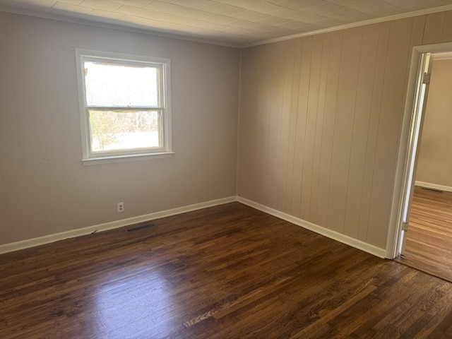 empty room with baseboards, visible vents, dark wood-style flooring, and crown molding