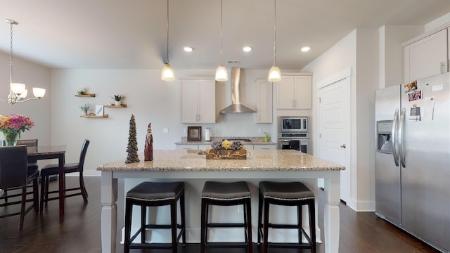 kitchen featuring appliances with stainless steel finishes, a kitchen island, white cabinets, pendant lighting, and wall chimney range hood