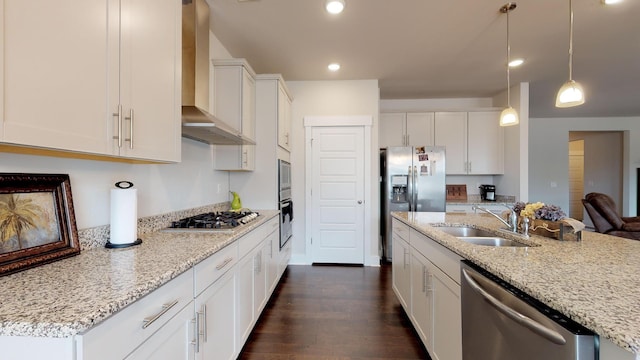 kitchen with appliances with stainless steel finishes, sink, white cabinets, light stone countertops, and wall chimney exhaust hood