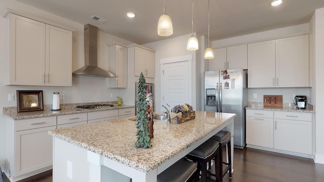 kitchen featuring pendant lighting, stainless steel appliances, white cabinets, a center island with sink, and wall chimney exhaust hood