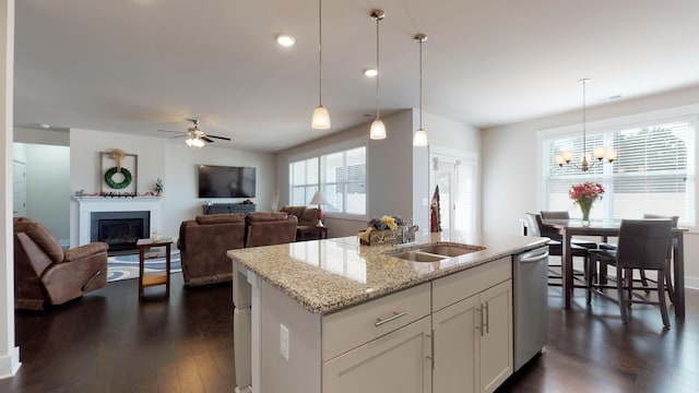 kitchen with pendant lighting, white cabinets, a kitchen island with sink, stainless steel dishwasher, and light stone counters