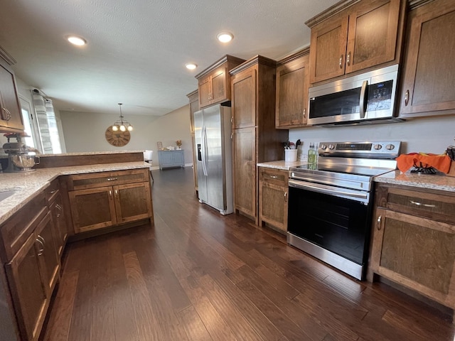 kitchen featuring dark hardwood / wood-style floors, hanging light fixtures, stainless steel appliances, light stone countertops, and a textured ceiling