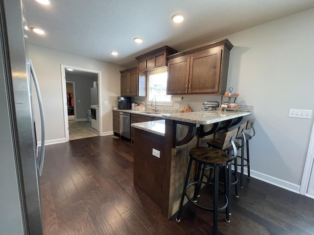 kitchen with sink, dark wood-type flooring, a breakfast bar, stainless steel appliances, and light stone countertops