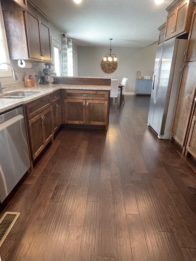 kitchen with appliances with stainless steel finishes, dark hardwood / wood-style floors, pendant lighting, sink, and kitchen peninsula