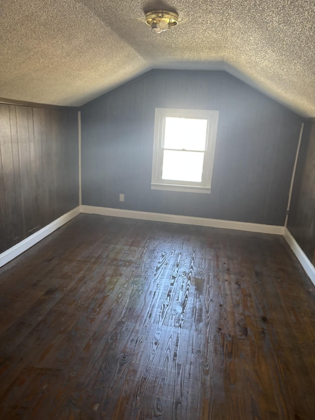 additional living space featuring dark wood-type flooring, a textured ceiling, and vaulted ceiling