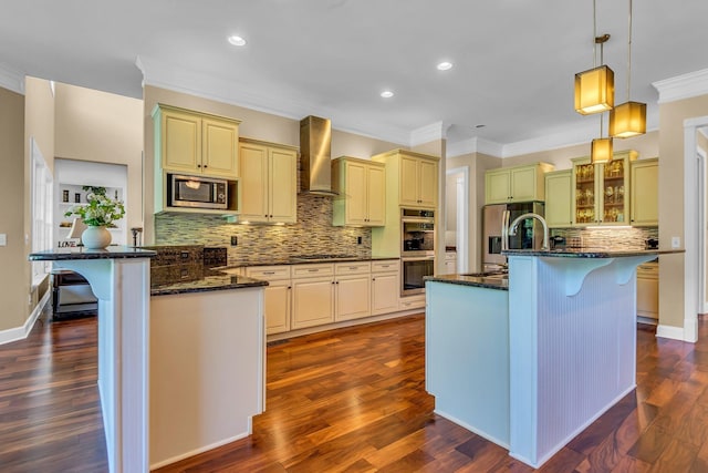 kitchen featuring an island with sink, appliances with stainless steel finishes, a breakfast bar area, and wall chimney range hood