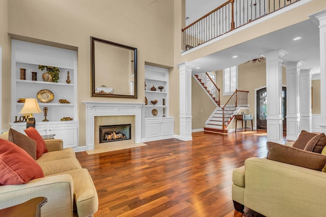 living room featuring dark wood-type flooring, a high end fireplace, built in features, and ornate columns