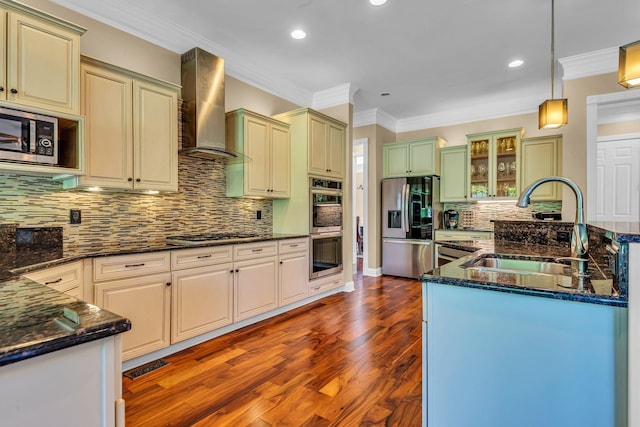 kitchen featuring wall chimney range hood, sink, hanging light fixtures, stainless steel appliances, and dark stone counters