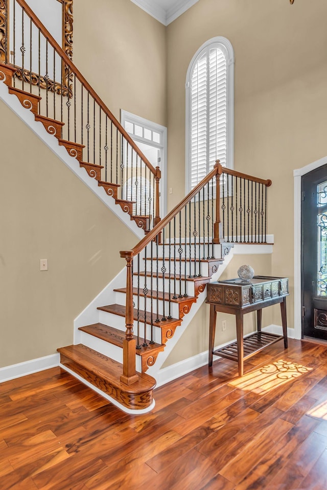 staircase with hardwood / wood-style floors, a towering ceiling, and ornamental molding