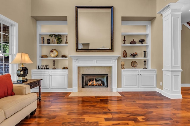 living room featuring a high end fireplace, built in features, decorative columns, and dark hardwood / wood-style floors