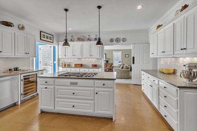 kitchen with appliances with stainless steel finishes, hanging light fixtures, wine cooler, ornamental molding, and white cabinets